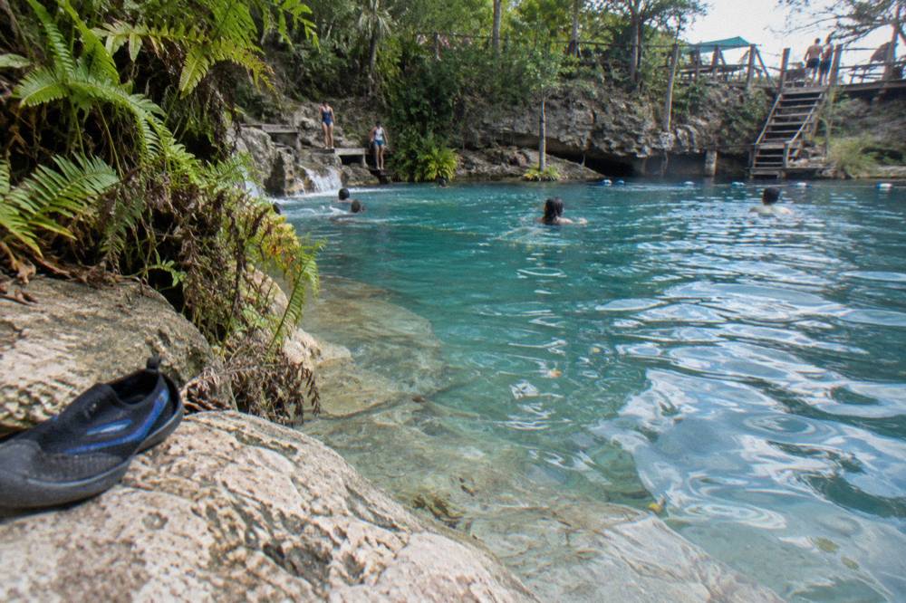Calm shallow edge of a blue pool where rocks slope gently into the water