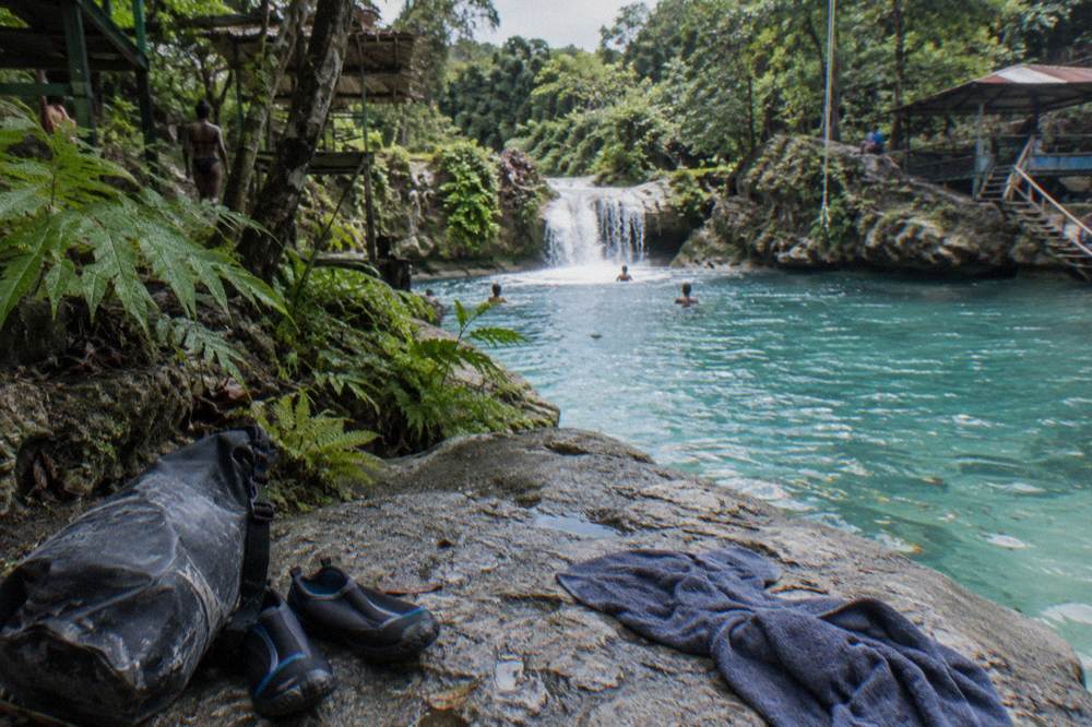 Water shoes and dry bag set on a rock beside a turquoise jungle pool