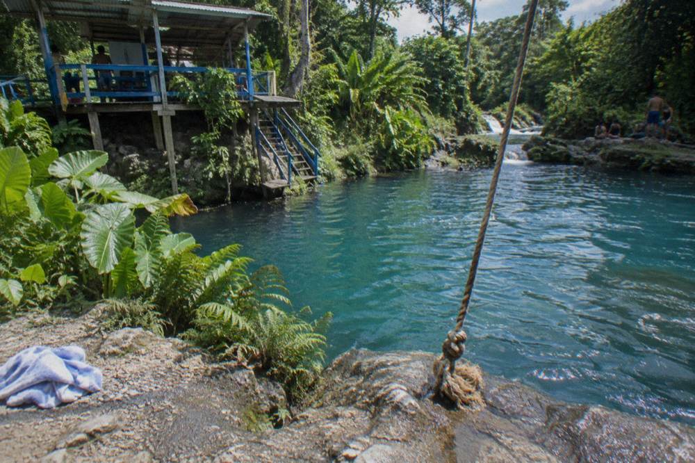 Rope swing hanging over a deep turquoise pool framed by greenery