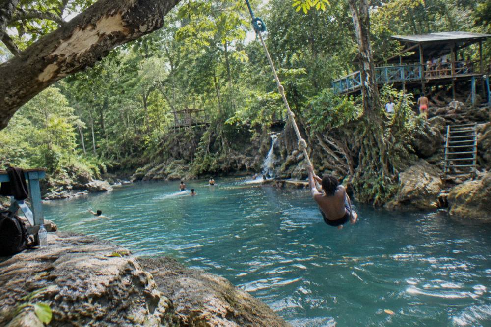 A rope swing hanging over a blue river pool beneath tall trees