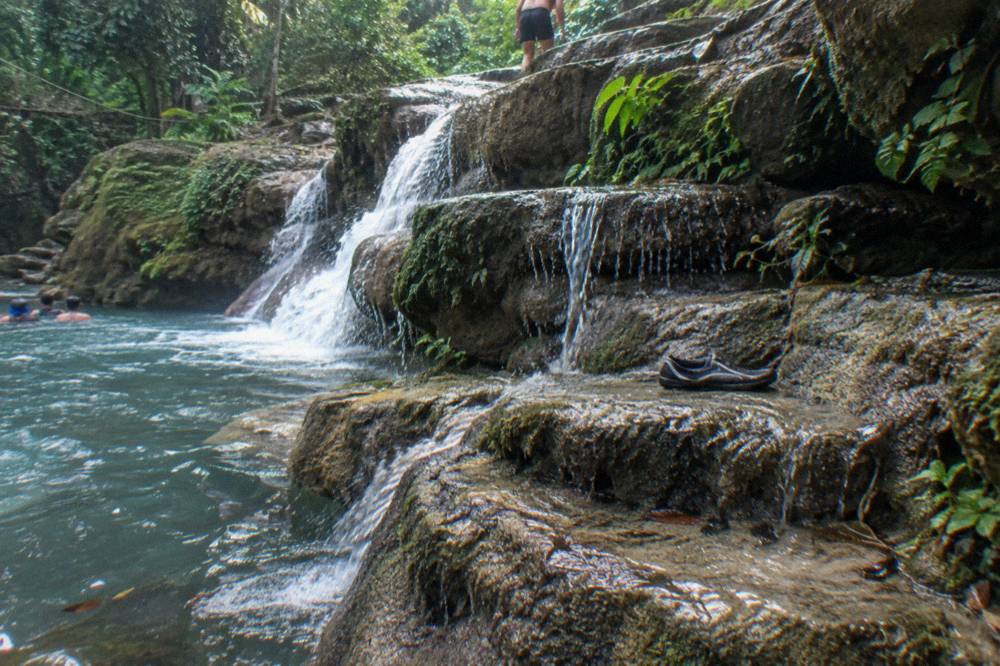 Layered limestone ledges beside a cascading waterfall in a green gorge