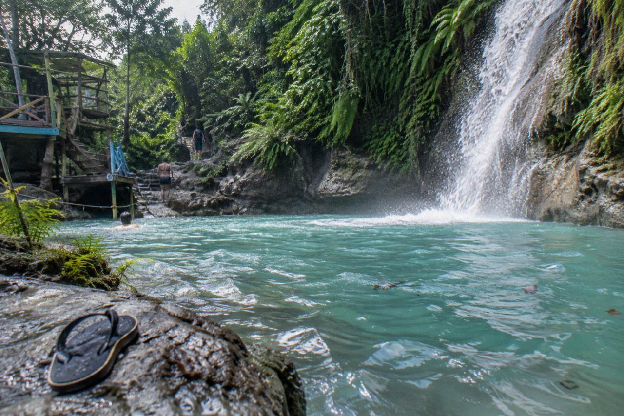 A turquoise pool at the base of a jungle waterfall surrounded by greenery