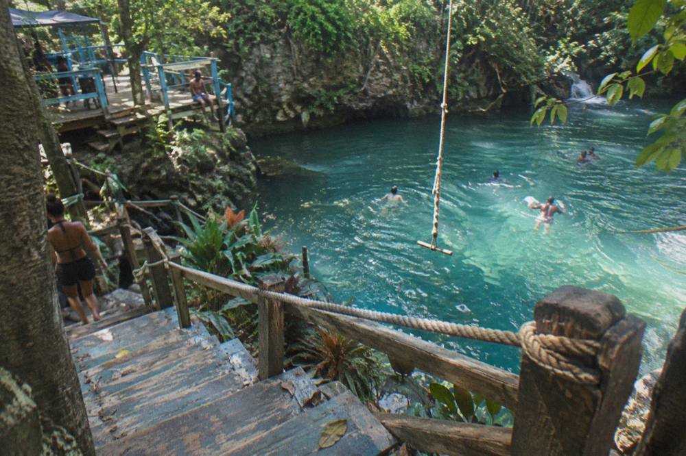 Wooden steps and rope swing over a turquoise jungle pool at a Jamaican waterfall
