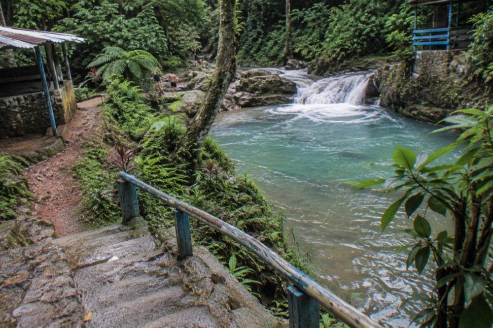Line of water shoes and towels on a bench beside a jungle waterfall path