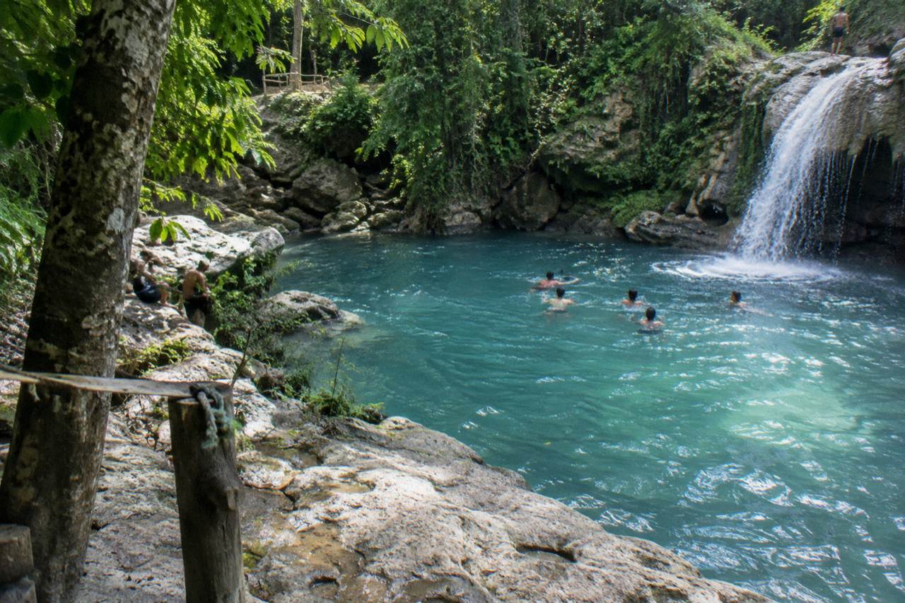 Turquoise waterfall pool ringed by limestone rocks and green forest