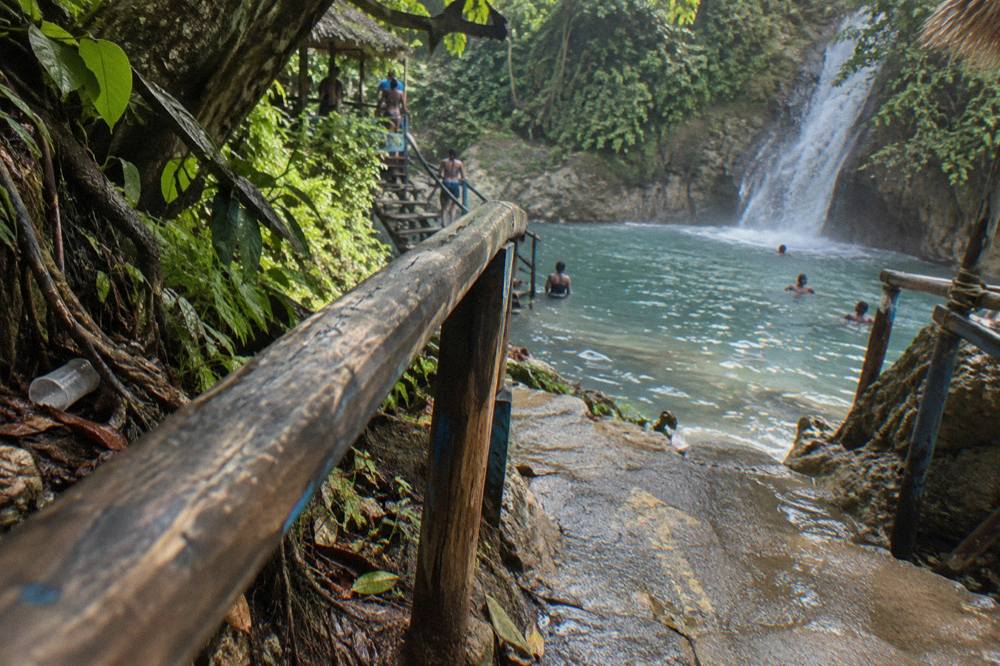 Wooden signs pointing toward waterfall pools along a jungle trail in Jamaica.