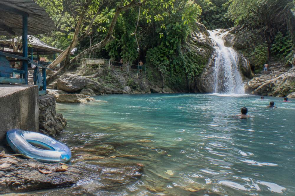 A waterfall cascading into a wide blue pool ringed by tropical trees.
