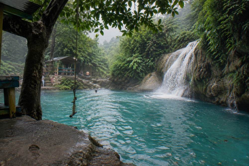 Turquoise pool at the base of a waterfall with rope swing hanging from an overhanging tree
