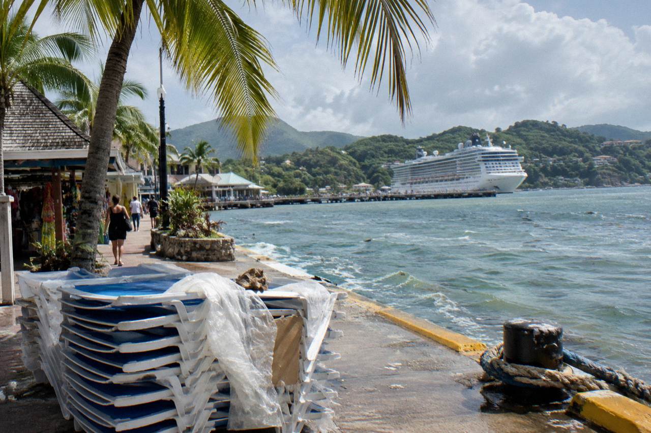 Cruise ship docked at a Caribbean port town with green hills rising behind the harbor