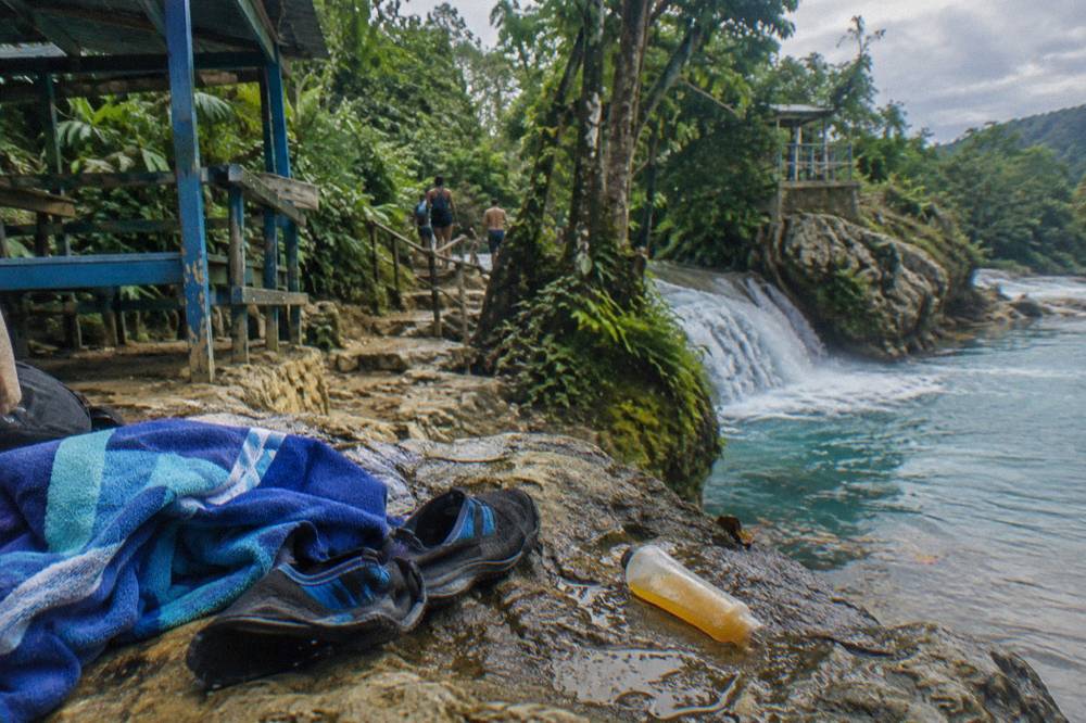Water shoes and towels drying on rocks beside a jungle waterfall trail