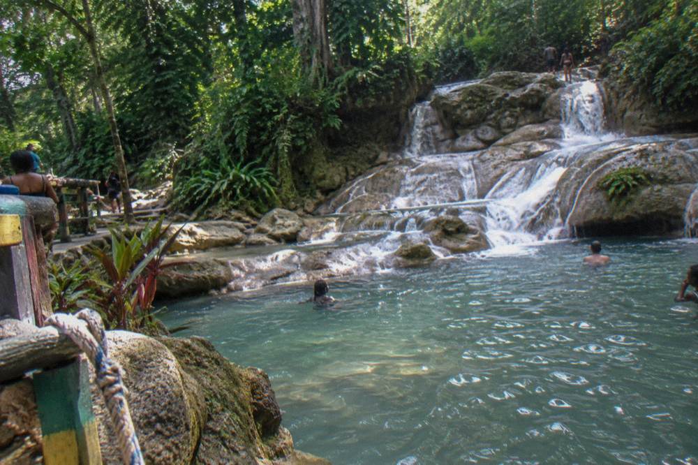 Cascading terraced waterfall flowing through tropical forest toward a boulder-lined pool