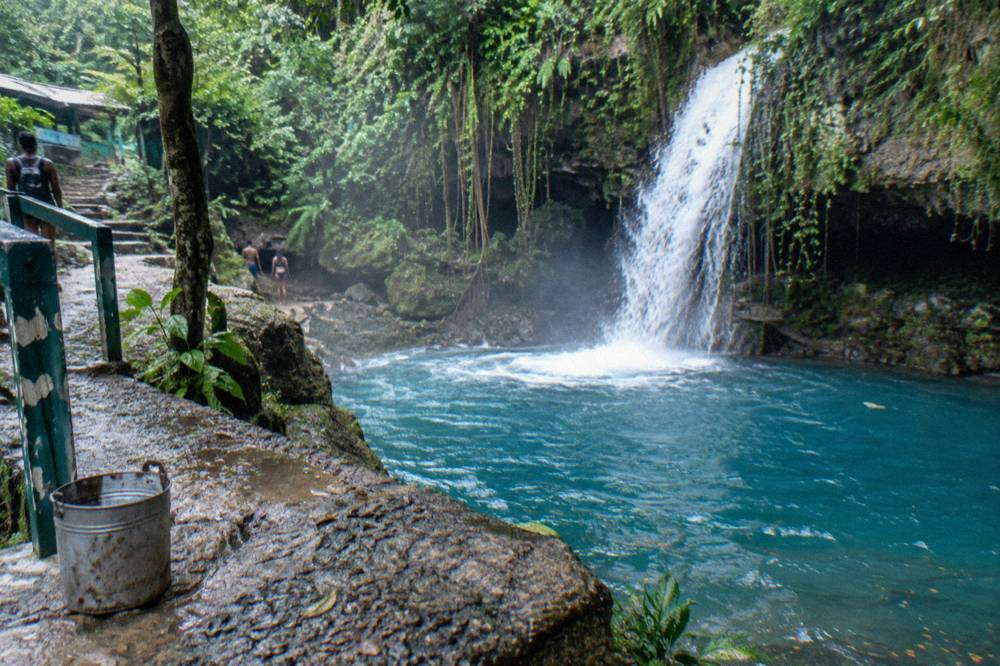 Waterfall cascading into a deep blue limestone pool framed by vines