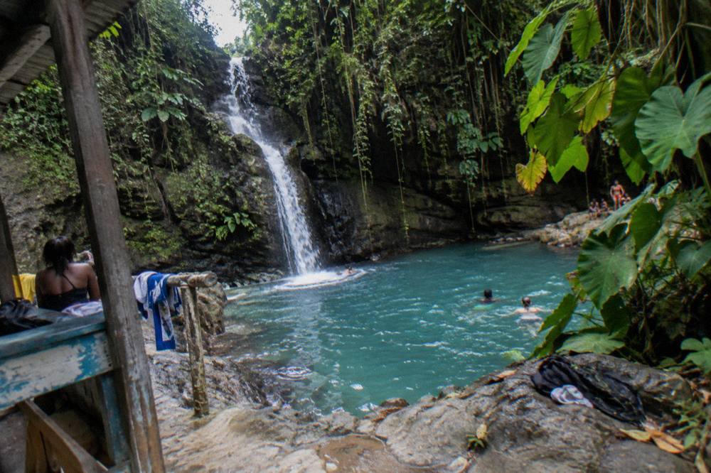 A narrow waterfall pouring into a bright turquoise pool framed by dense green jungle