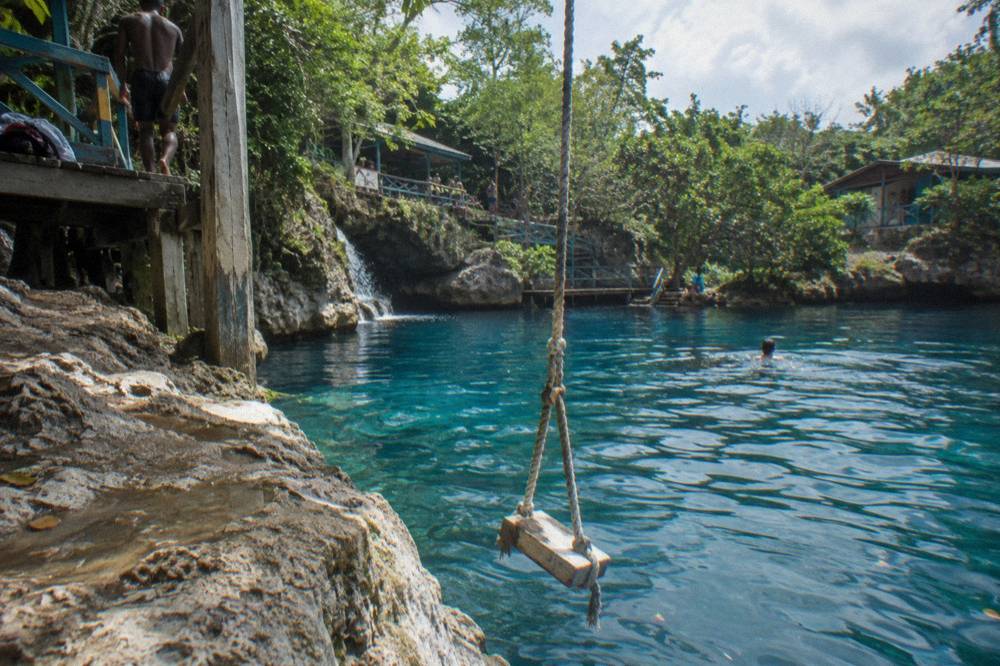 A rope swing hanging from a tree over a deep turquoise pool at a jungle waterfall