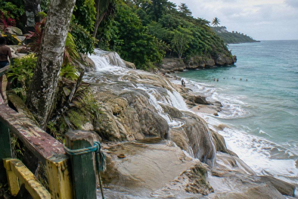 Cascading limestone waterfall terraces dropping toward a beach and calm Caribbean water