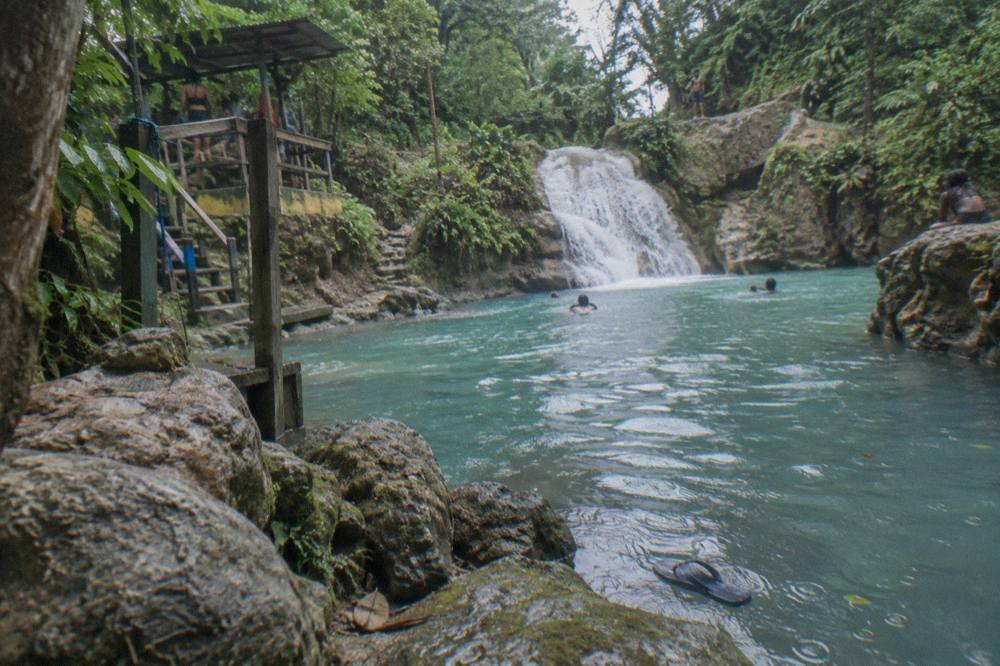 A turquoise swimming hole at the base of a jungle waterfall with limestone rocks