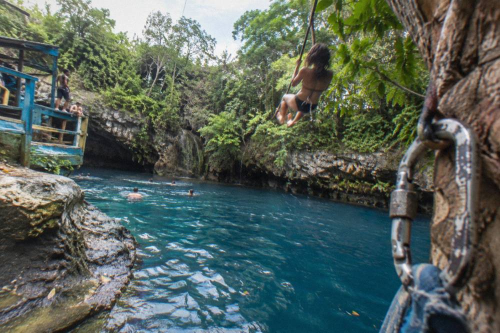 A traveler on a rope swing above a deep blue jungle pool
