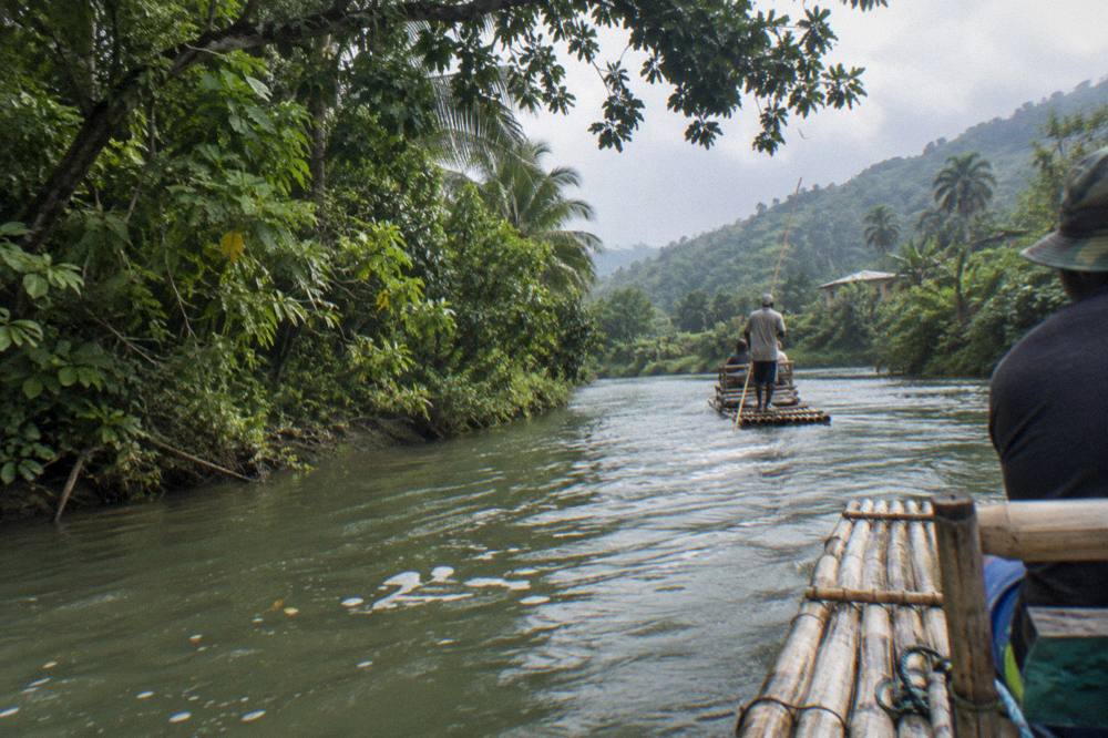 Two bamboo rafts floating down a calm green river between overhanging tropical trees