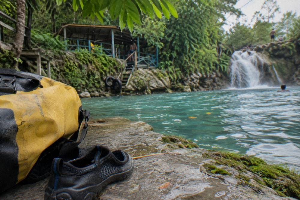 Water shoes and dry bag resting on a rock beside a turquoise pool