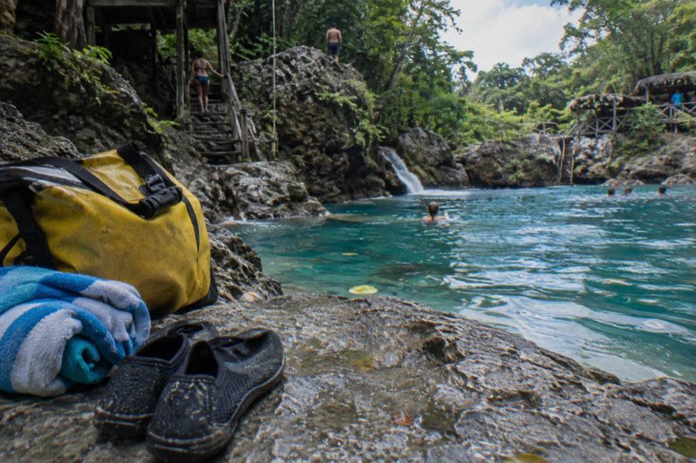 Water shoes, towels and a dry bag arranged on a wooden bench beside a jungle pool