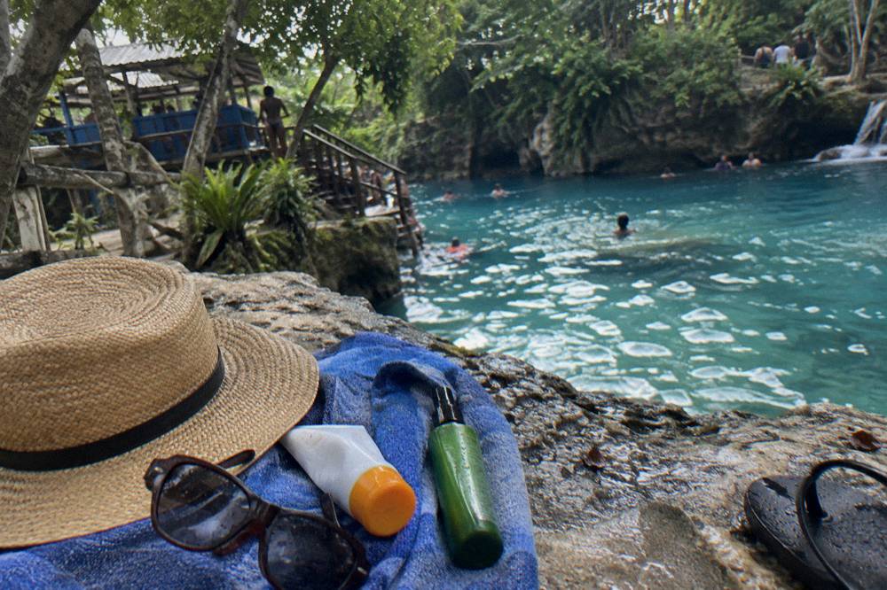 Sunscreen and insect repellent bottles on a towel with sunglasses and a hat
