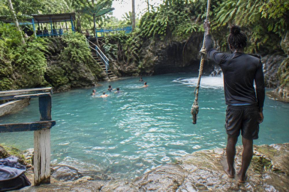 Guide on a rock ledge beside a rope swing speaking to visitors in a jungle pool