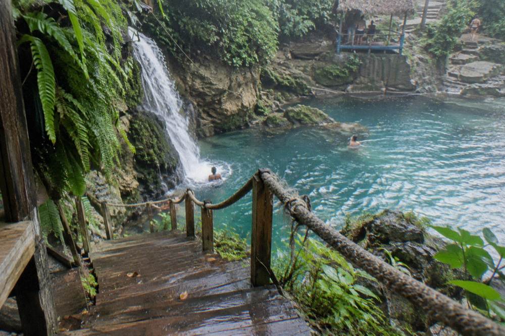 Wooden steps and a handrail descending beside a small waterfall to a blue pool
