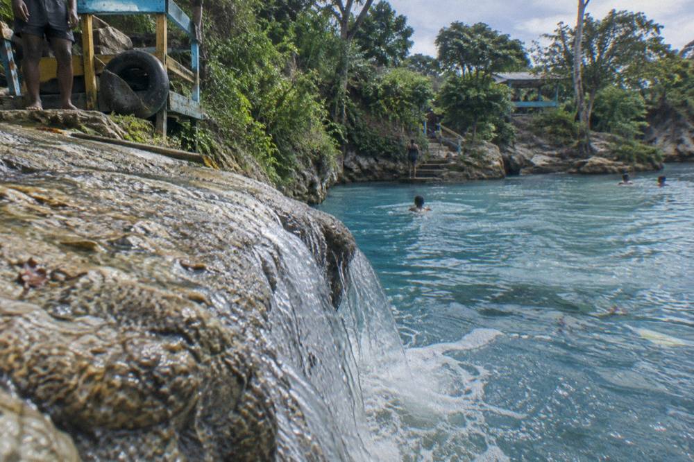 Waterfall pouring over limestone ledge into a clear blue swimming hole