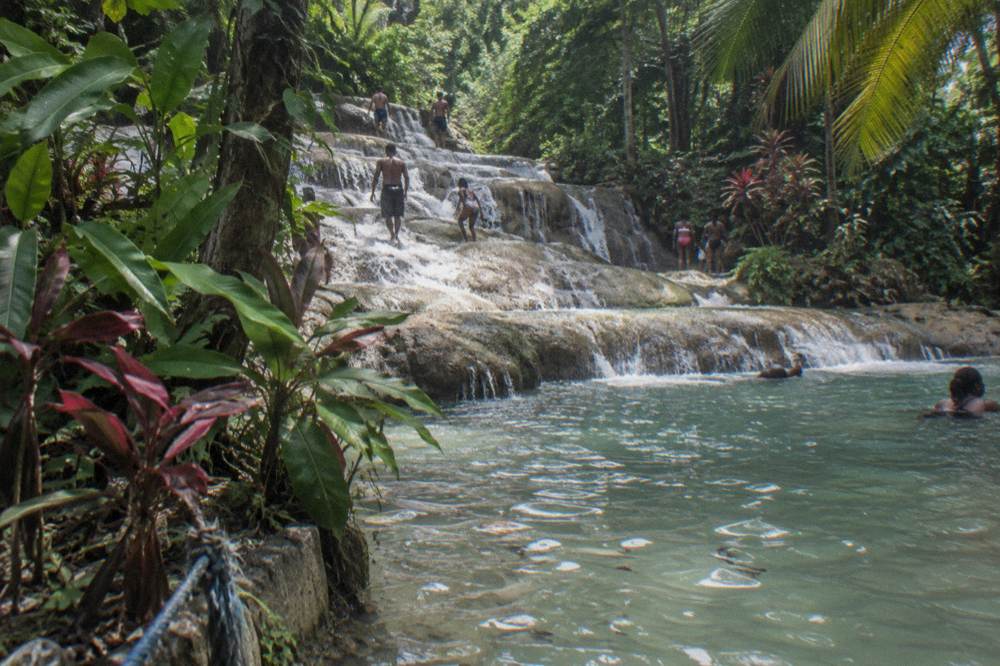 Terraced waterfall cascading through tropical gardens with visitors on the rocks