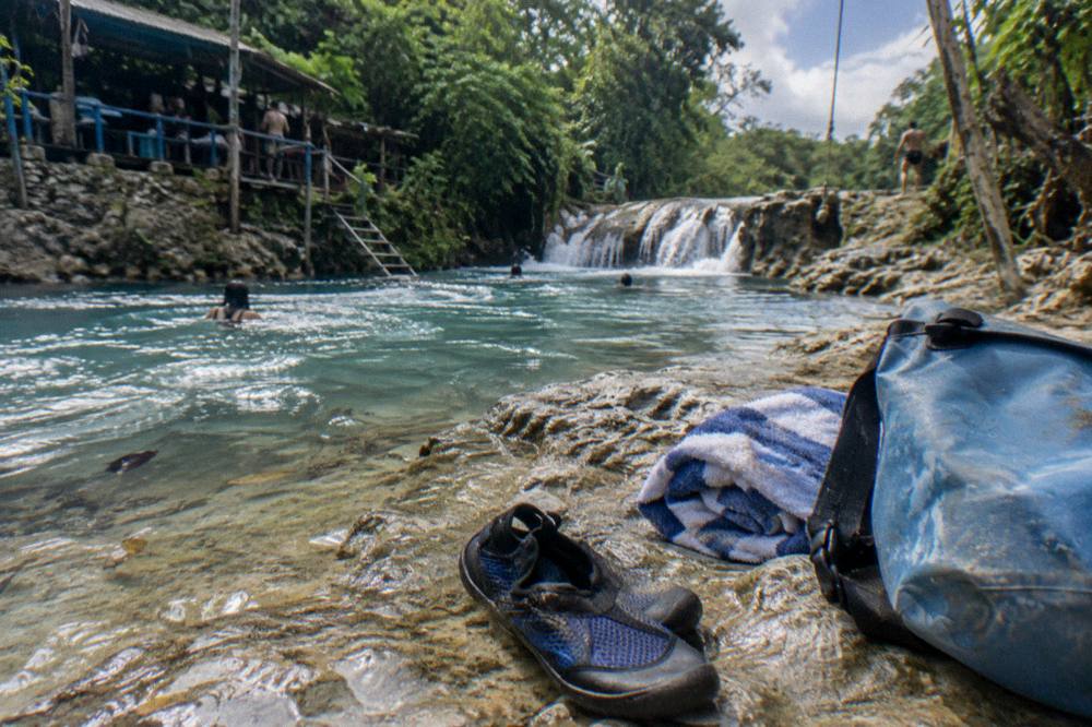 Water shoes, towel and dry bag resting on a rock beside a jungle stream