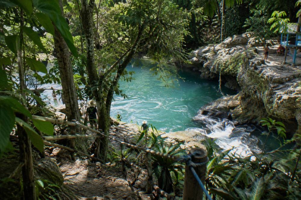 Turquoise waterfall pool framed by limestone ledges and overhanging jungle foliage