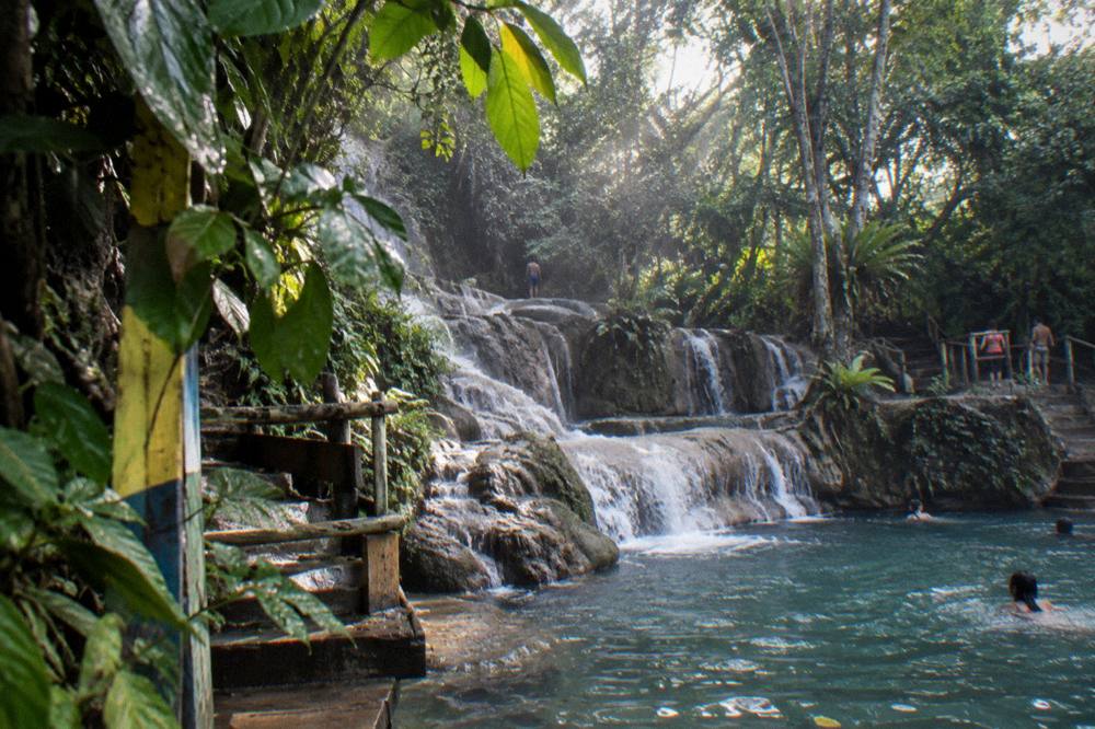Sunlight reaching through jungle canopy onto a cascade of small waterfalls