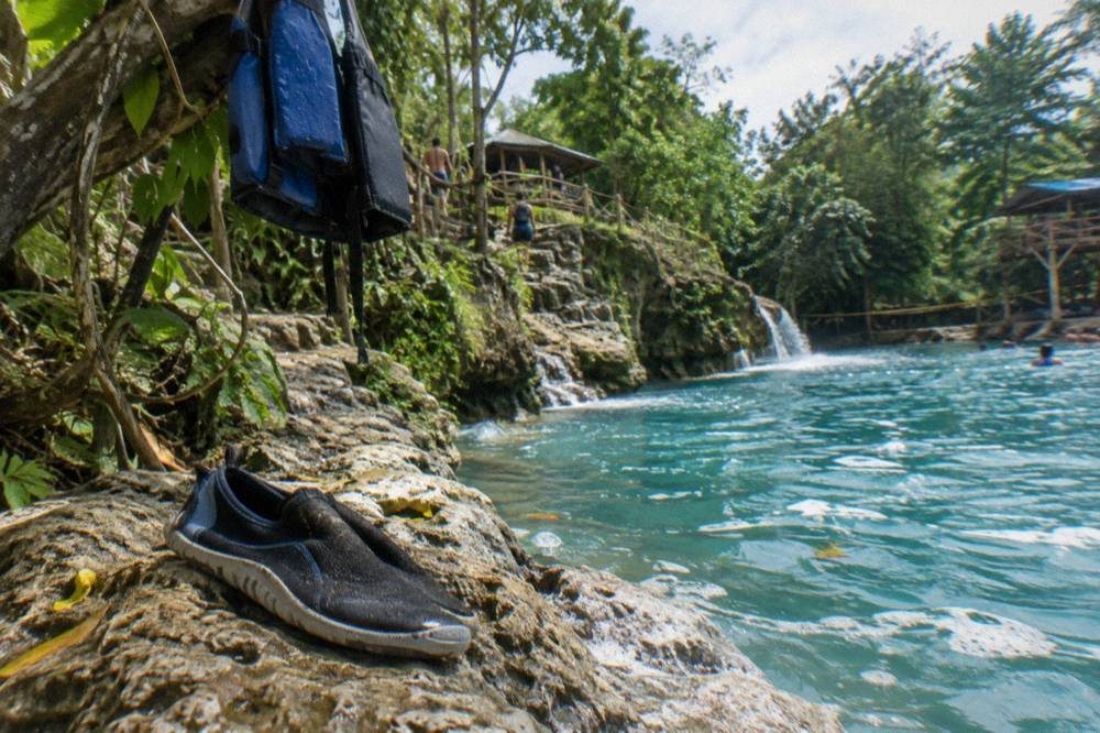 Pair of water shoes resting on a rock beside clear blue water