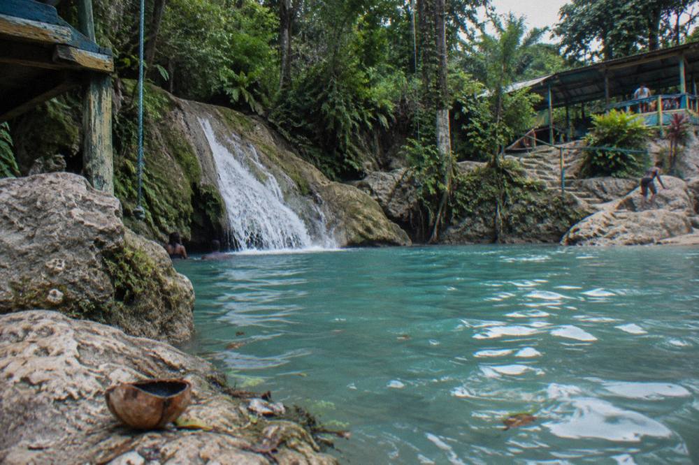 Clear turquoise pool at the base of a jungle waterfall with limestone rocks