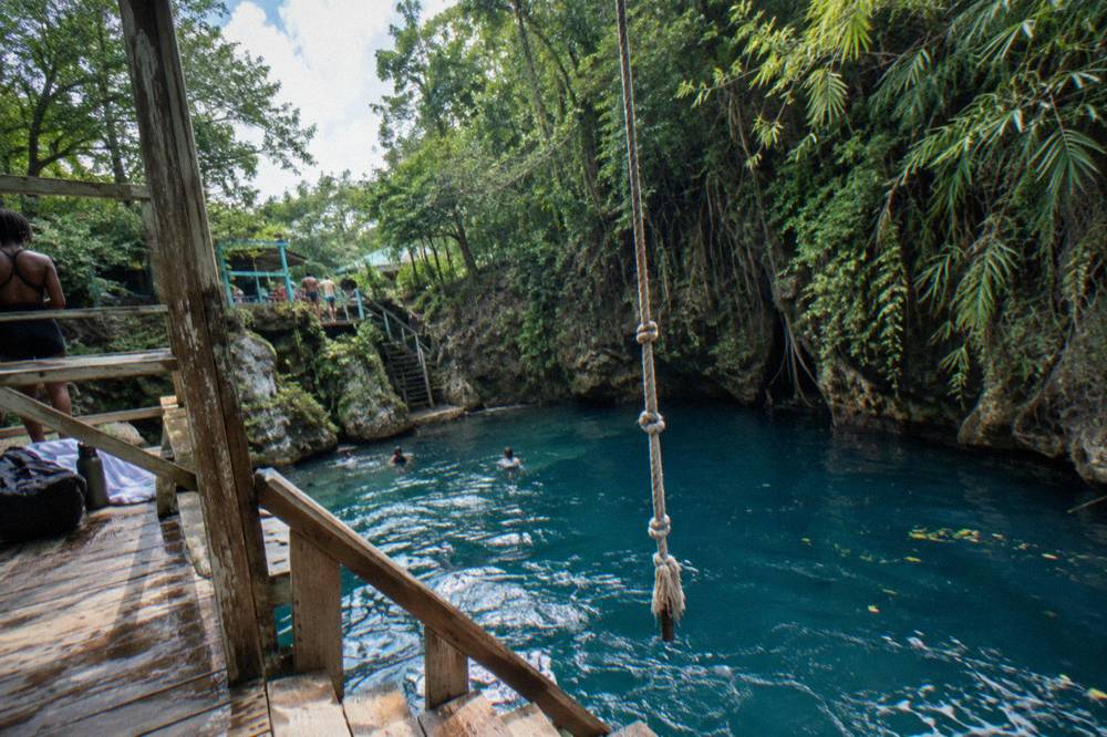 Wooden rope swing hanging over a blue swimming hole in a green canyon