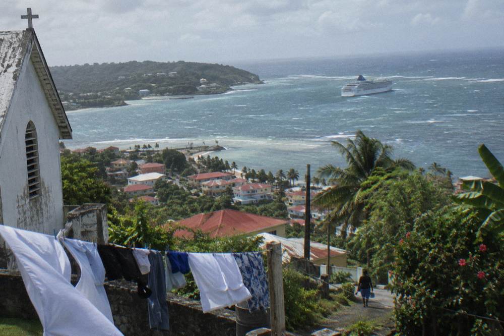 Cruise ship anchored off a green coastline near a small port town