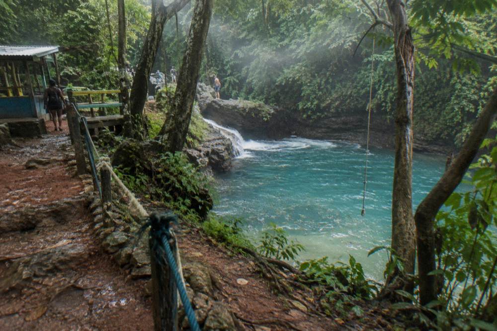 Wooden sign beside a jungle trail leading toward a waterfall swimming hole