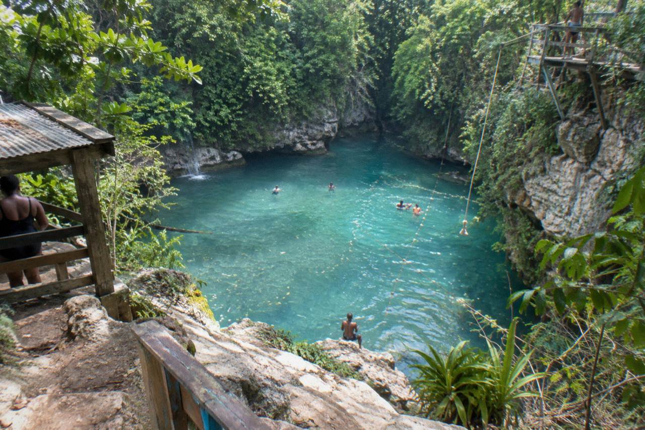 Turquoise waterfall pool ringed by forested limestone cliffs at the Blue Hole near Ocho Rios