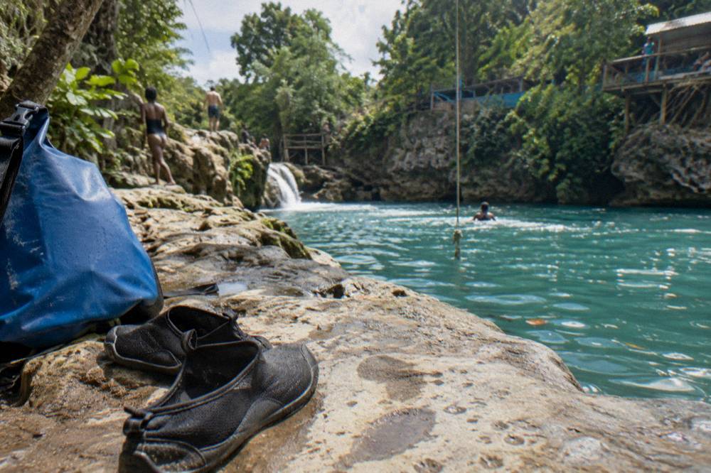 Pair of water shoes and a dry bag on a rock beside a turquoise pool