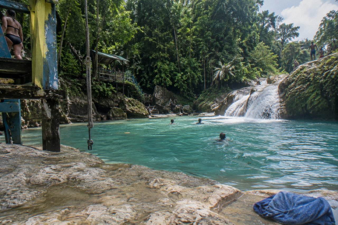 Turquoise waterfall pool ringed by limestone rocks and dense green forest in Jamaica
