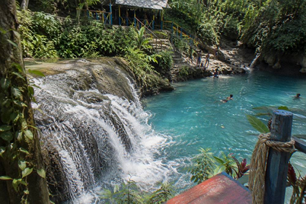 Waterfall cascading into a bright turquoise pool ringed by limestone and tropical plants
