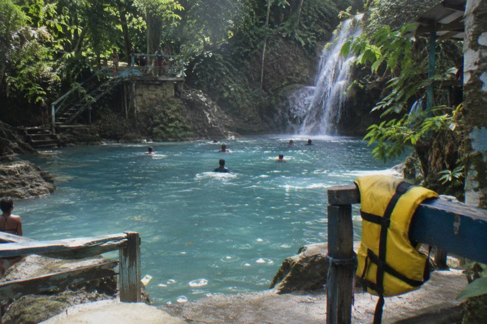 Swimmers in a bright blue natural pool below a jungle waterfall