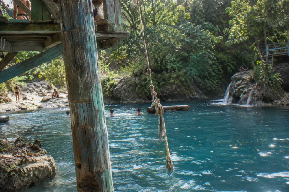 Wooden rope swing hanging over a deep blue jungle pool