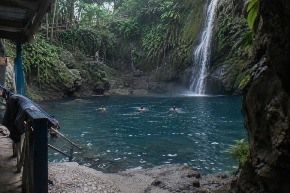 A waterfall cascading over stepped limestone rocks into a clear blue pool surrounded by rainforest