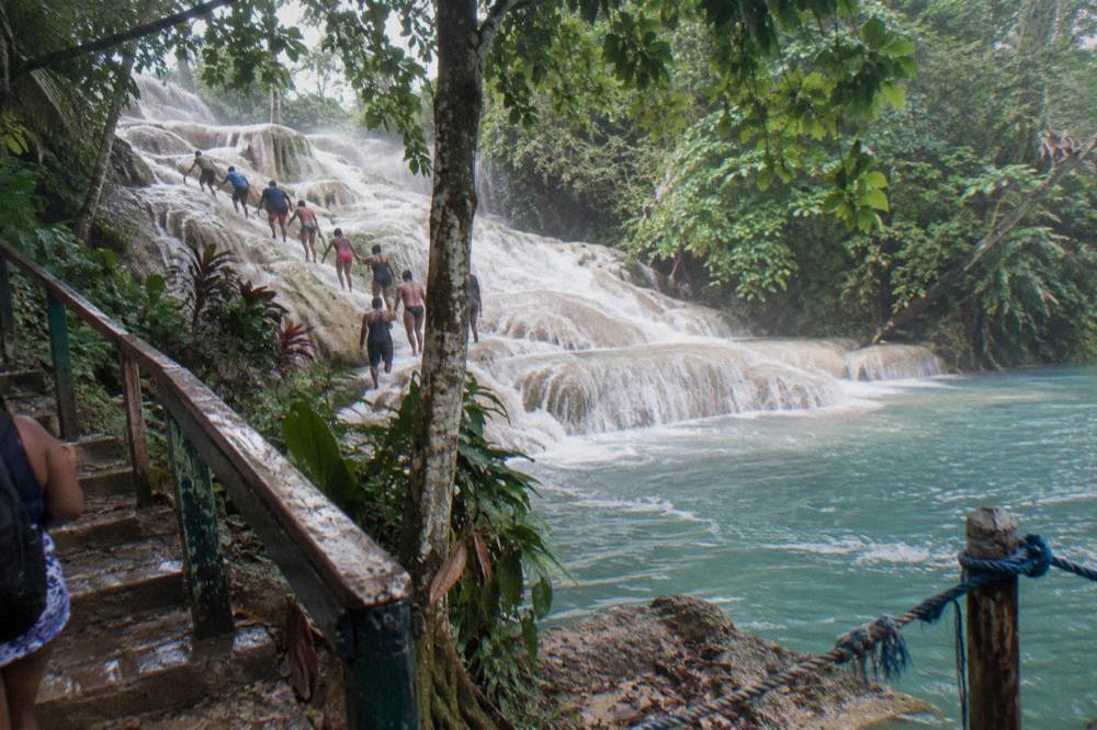 Visitors climbing a terraced limestone waterfall in a line holding hands