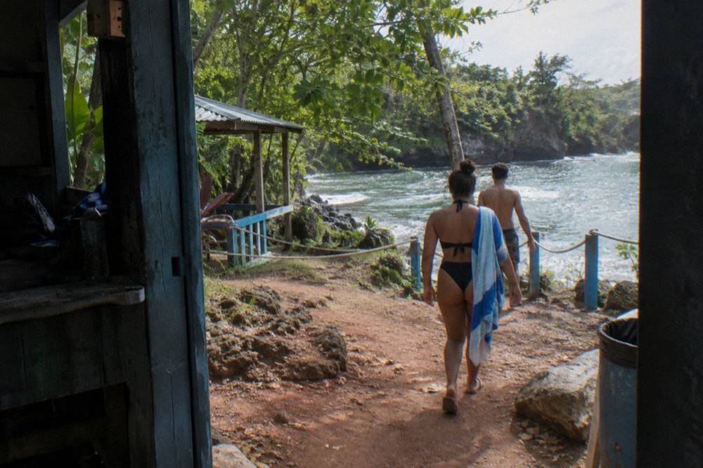 Travelers in swimwear walking a jungle path toward a waterfall pool