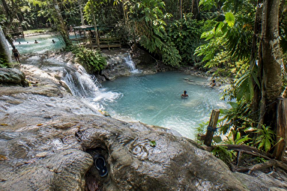 Waterfall pools flowing through lush green forest under bright morning light