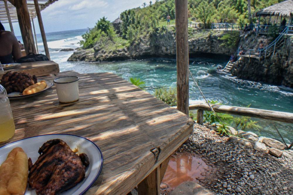 Wooden table with Jamaican jerk chicken and festival sides at an open-air food stop