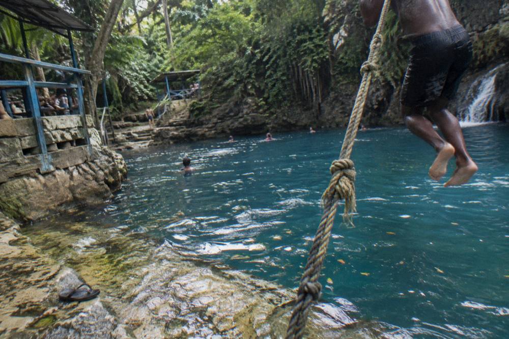 Rope swing hanging over a deep blue jungle pool at a Jamaican waterfall