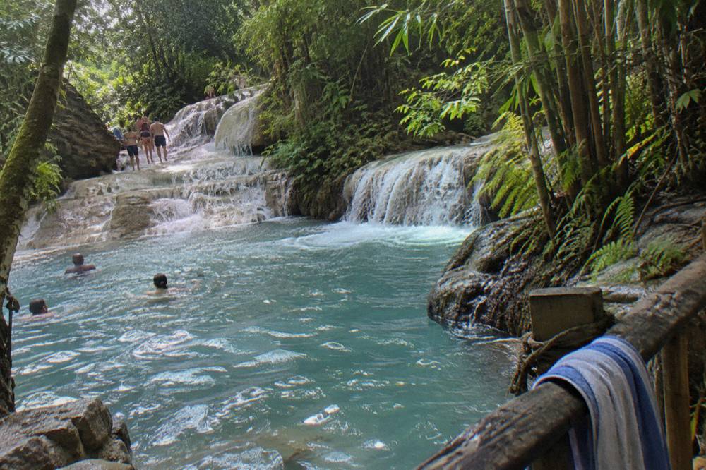 Terraced limestone waterfall with water cascading into a pool ringed by trees